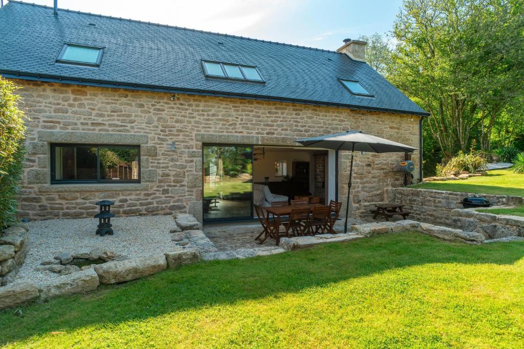 a stone house with a patio and an umbrella at Le Paradis Perdu - Maison avec jardin paysagé in Quistinic
