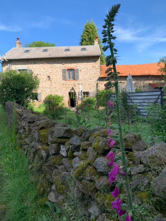 a stone wall in front of a house with purple flowers at Lavande in Châtelus-le-Marcheix