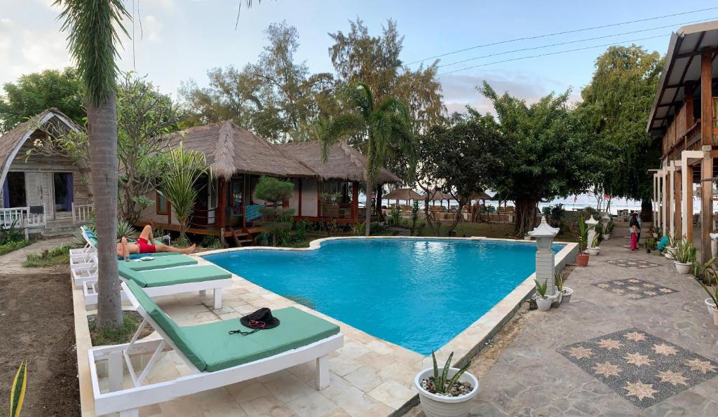 a swimming pool with two lounge chairs next to a house at Biba Beach Village in Gili Islands