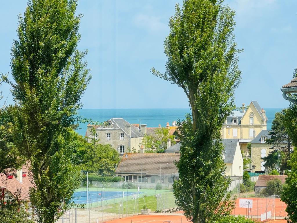 a view of a tennis court between two trees at Maison vue mer 4 personnes in Arromanches-les-Bains