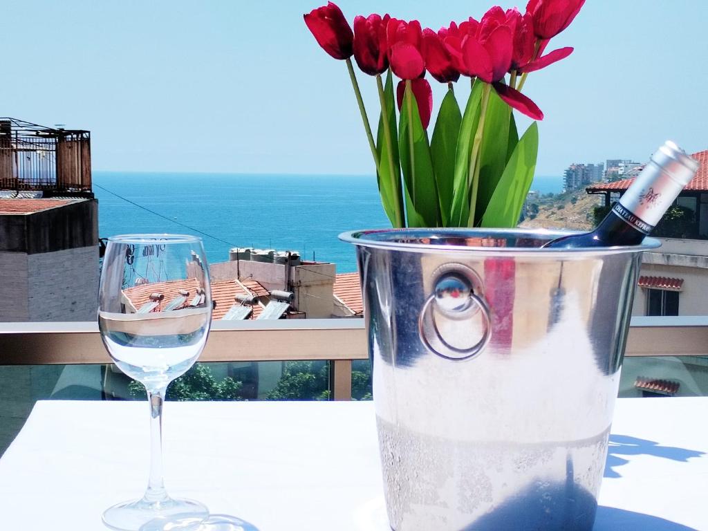 a glass of wine and a vase with red flowers at Mateus Hotel in Jounieh