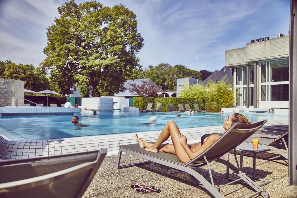 a woman sitting in a chair next to a swimming pool at Mondorf Parc Hotel & Spa in Mondorf-les-Bains
