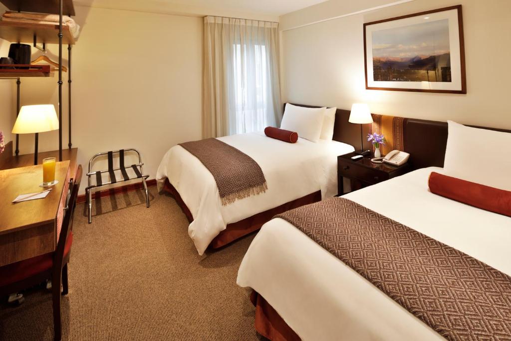 a hotel room with two beds and a desk at LP Los Portales Hotel Cusco in Cusco