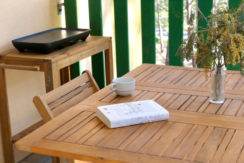 a wooden table with a book and a cup on it at Apt Les Grands Pins, entre Forêt, Lac et Océan in Carcans