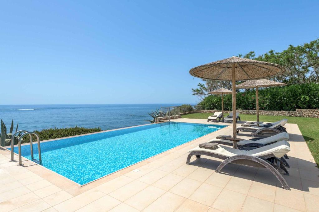 a swimming pool with chairs and an umbrella and the ocean at Paradise Beach II in Kiotari