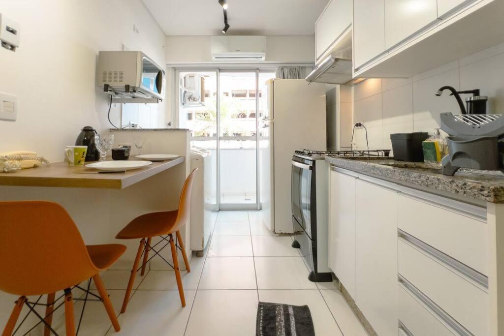 a white kitchen with a counter and chairs in it at Apto Piscina Academia Ar Cond CID108C in Maringá