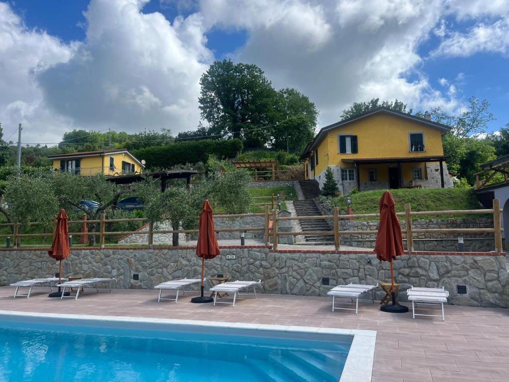a swimming pool with two umbrellas and benches next to a house at Podere il Glicine Wellness Charme & Relax in Fresonara