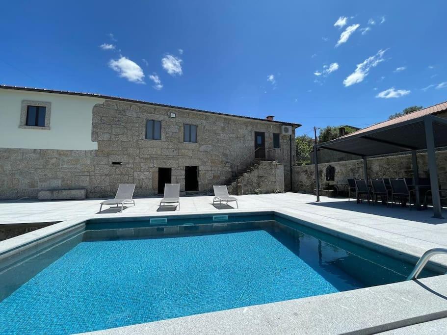 a swimming pool with two chairs and a house at Casa Curto in Terras de Bouro