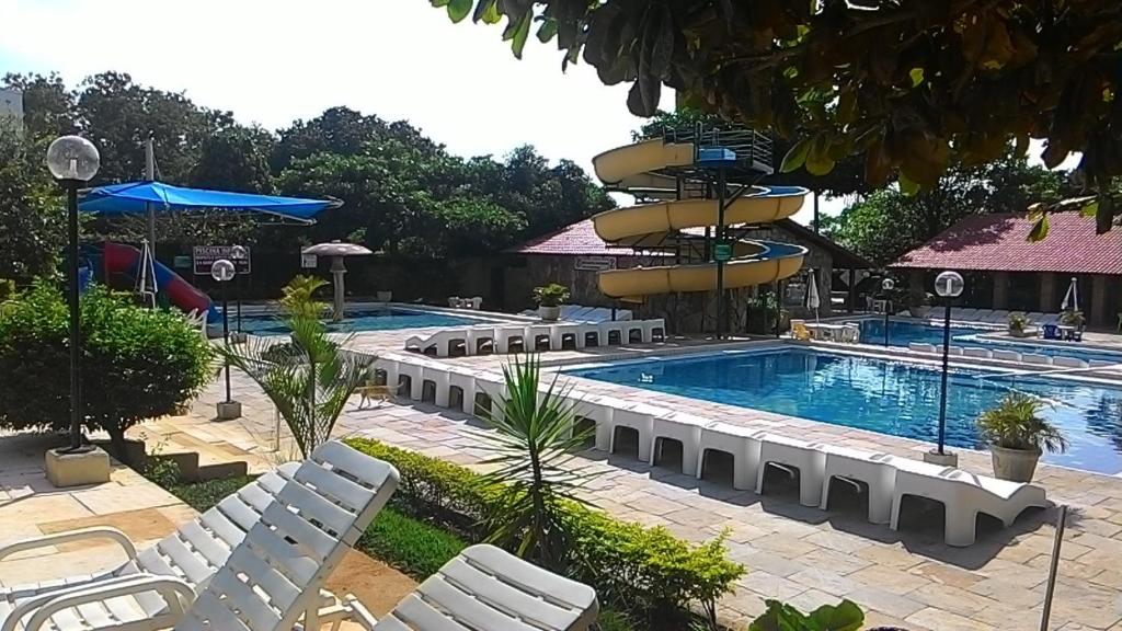 una piscina en un complejo con sillas blancas y una piscina en Império Romano Caldas Novas com piscinas 24h, e diRoma Acqua Park e Splash, en Caldas Novas