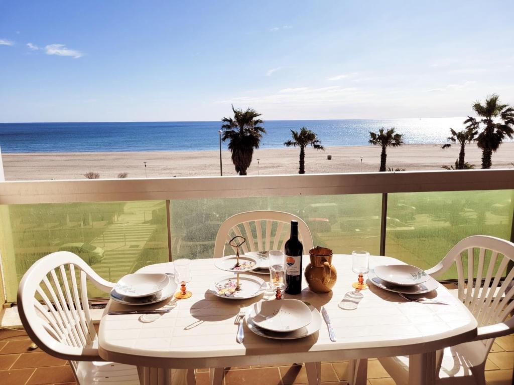 une table avec des chaises et une bouteille de vin et la plage dans l'établissement Canet-en-Roussillon - T2 lumineux pour 4 pers, terrasse, parking privé, plage à 50m - FR-1-794-114, à Canet