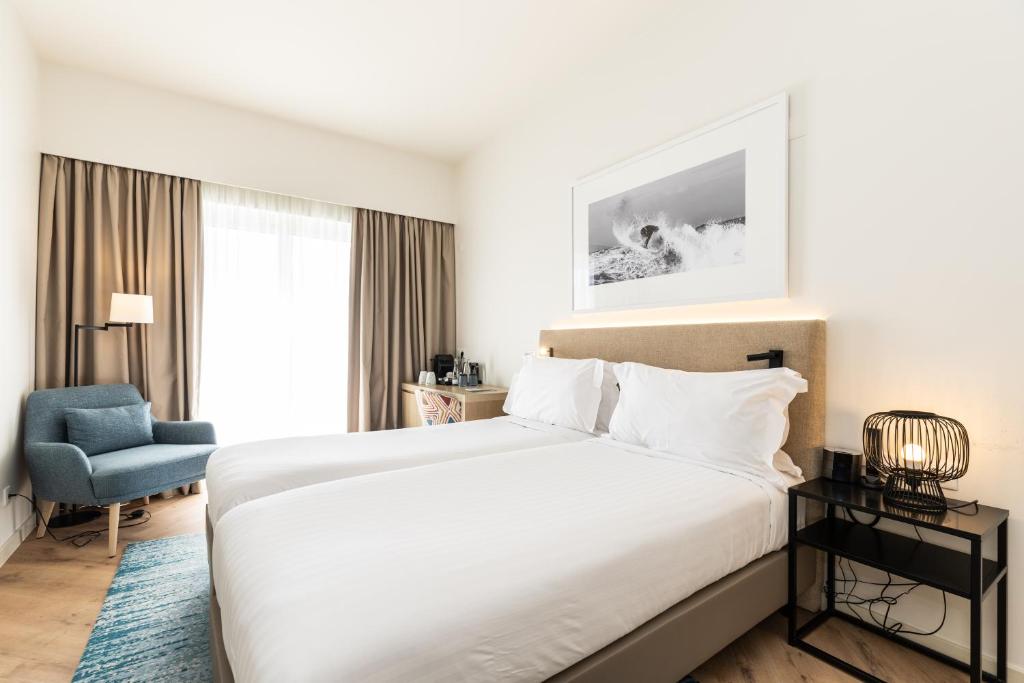 a bedroom with a large bed and a blue chair at Crowne Plaza - Caparica Lisbon in Costa da Caparica