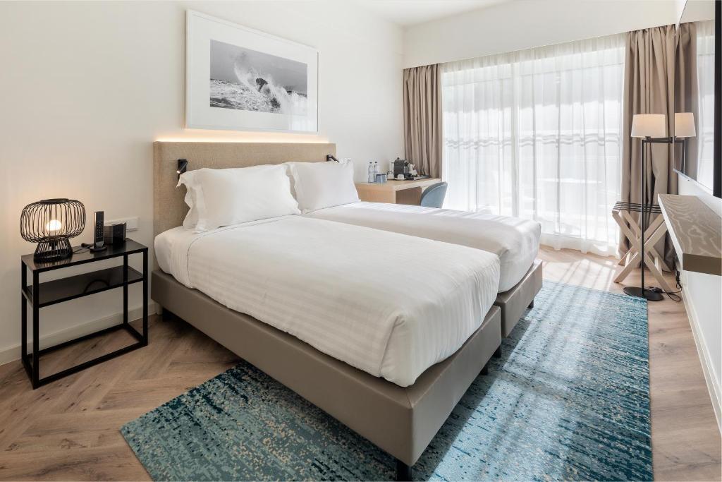 a bedroom with a large white bed with a blue rug at Crowne Plaza - Caparica Lisbon in Costa da Caparica