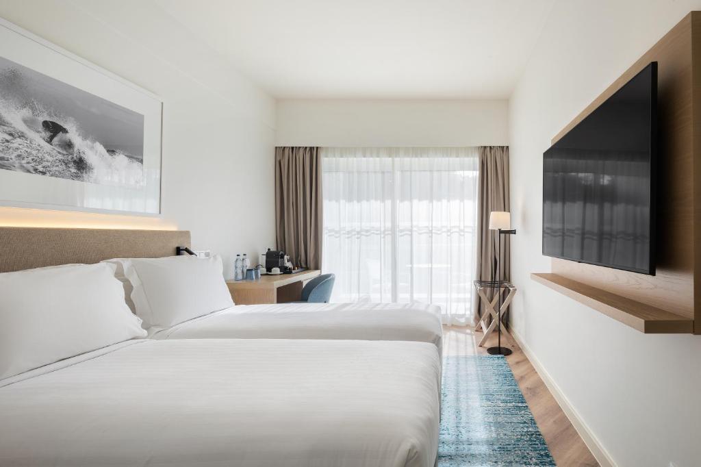 a hotel room with two beds and a flat screen tv at Crowne Plaza - Caparica Lisbon in Costa da Caparica