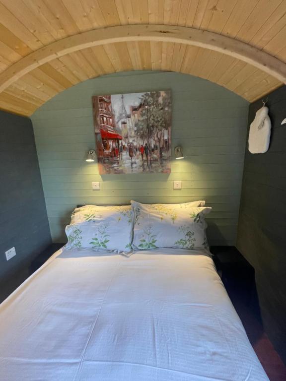 a bedroom with a white bed with a painting on the wall at Jackdaws Shepherds Hut in Epwell