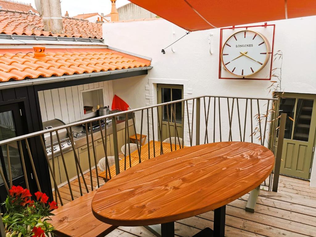 un banc en bois assis sur un balcon avec une horloge dans l'établissement La Maison de la Sirene, à Les Sables-dʼOlonne