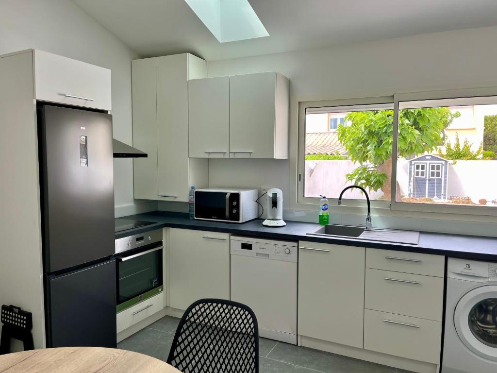 une cuisine avec des armoires blanches, un évier et une fenêtre dans l'établissement Villa Maurice, à Valras-Plage