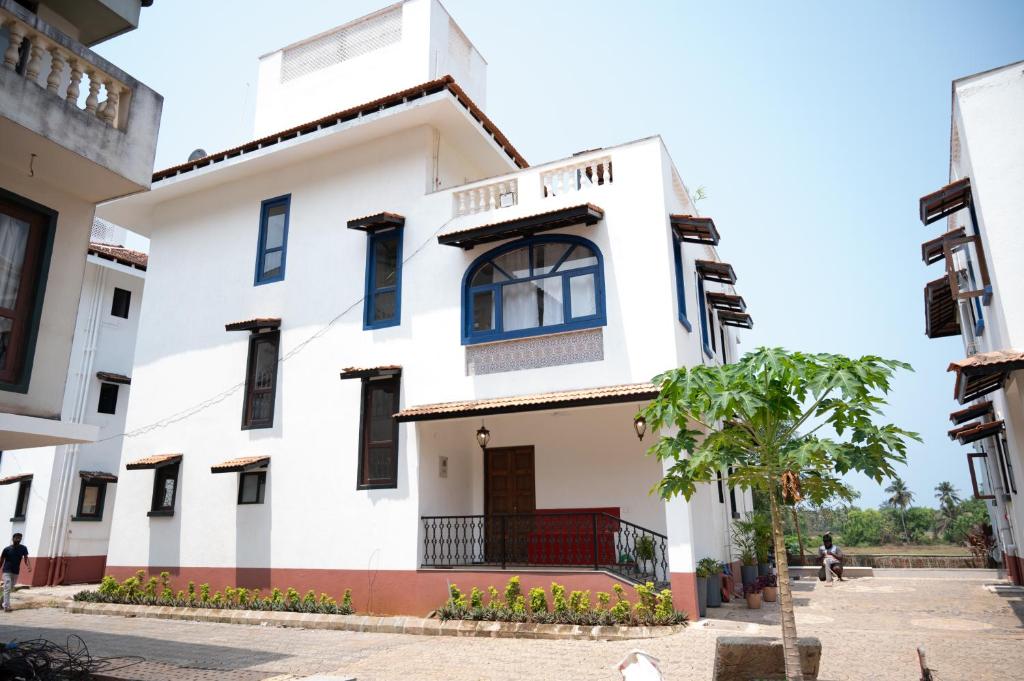 um edifício branco com janelas azuis e uma árvore em TERRA VERDE ! A Sunset Villa at Varca, South Goa ! em Varca