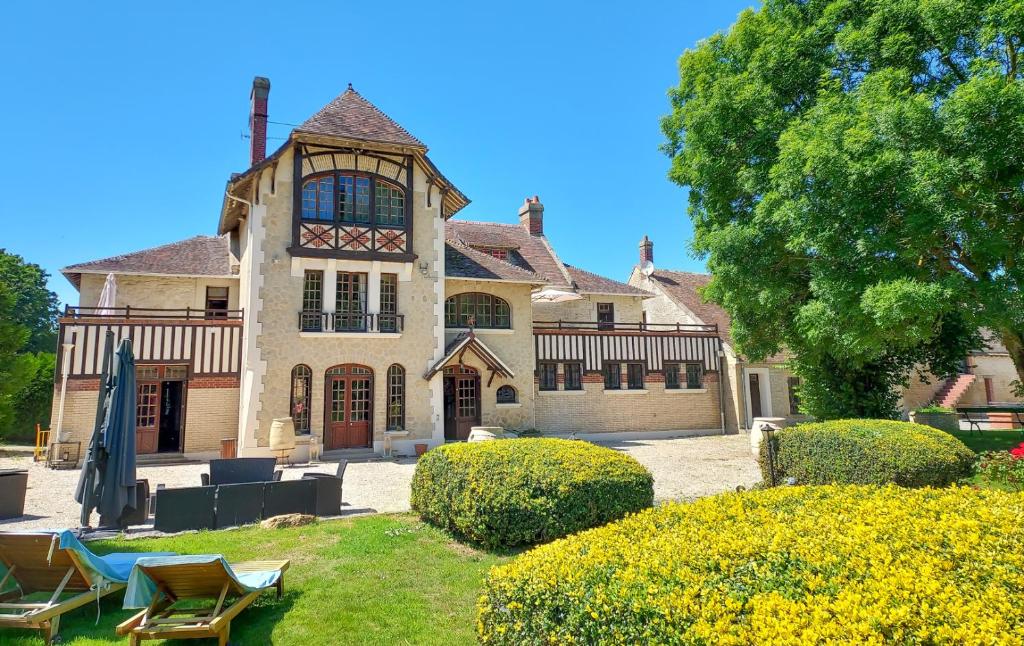 une grande maison avec une cour avec des chaises et des arbres dans l'établissement Le Haras des Charmilles, à Varaville
