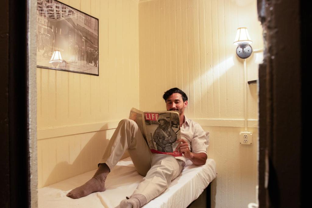 Un uomo seduto su un letto che legge un libro di The Nolita Express Hostel a New York
