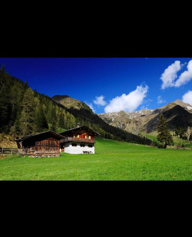 a house in a green field with mountains in the background at Peintnerhof Almhütte in Innervillgraten