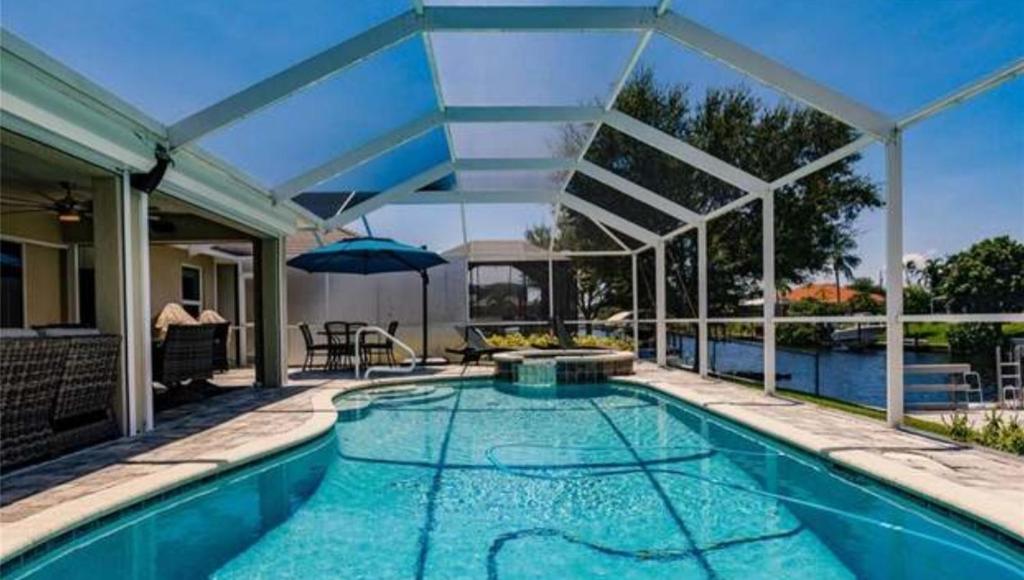 a swimming pool with an umbrella and a house at The Cape - Four Bedroom in Cape Coral