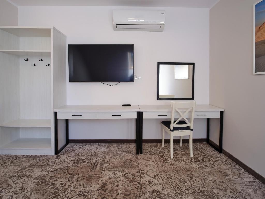White desk with drawers under wall-mounted TV and mirror, chair in minimalist hotel room.