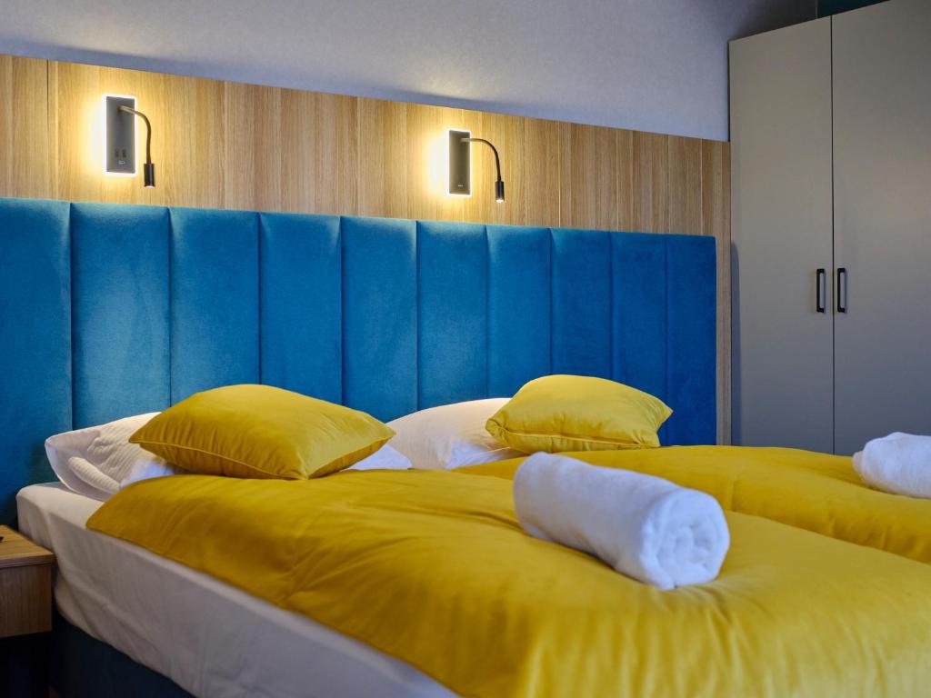 Twin beds with bright yellow duvets and pillows against a blue headboard, rolled towels.