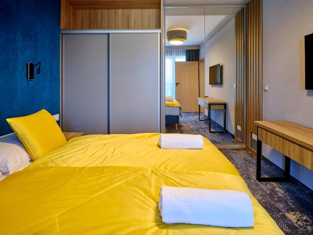 Yellow-bedded twin with mirrored wardrobe reflecting room, rolled towels on bed.