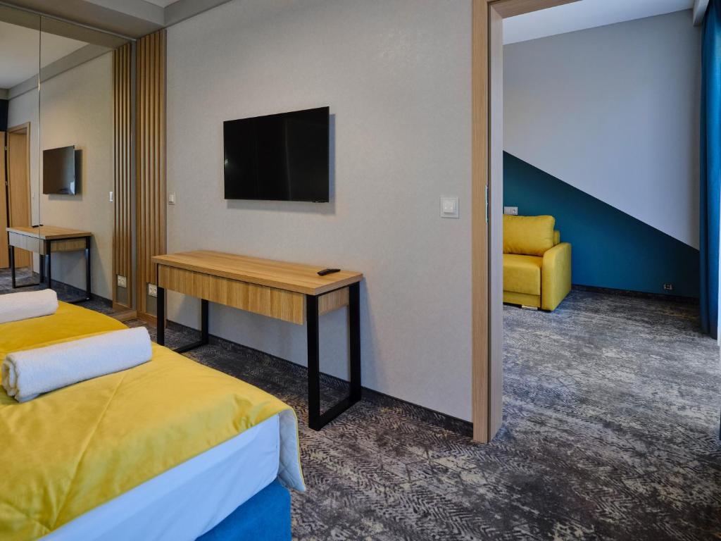Wall-mounted TV above wooden desk, doorway revealing yellow armchair in adjacent room.