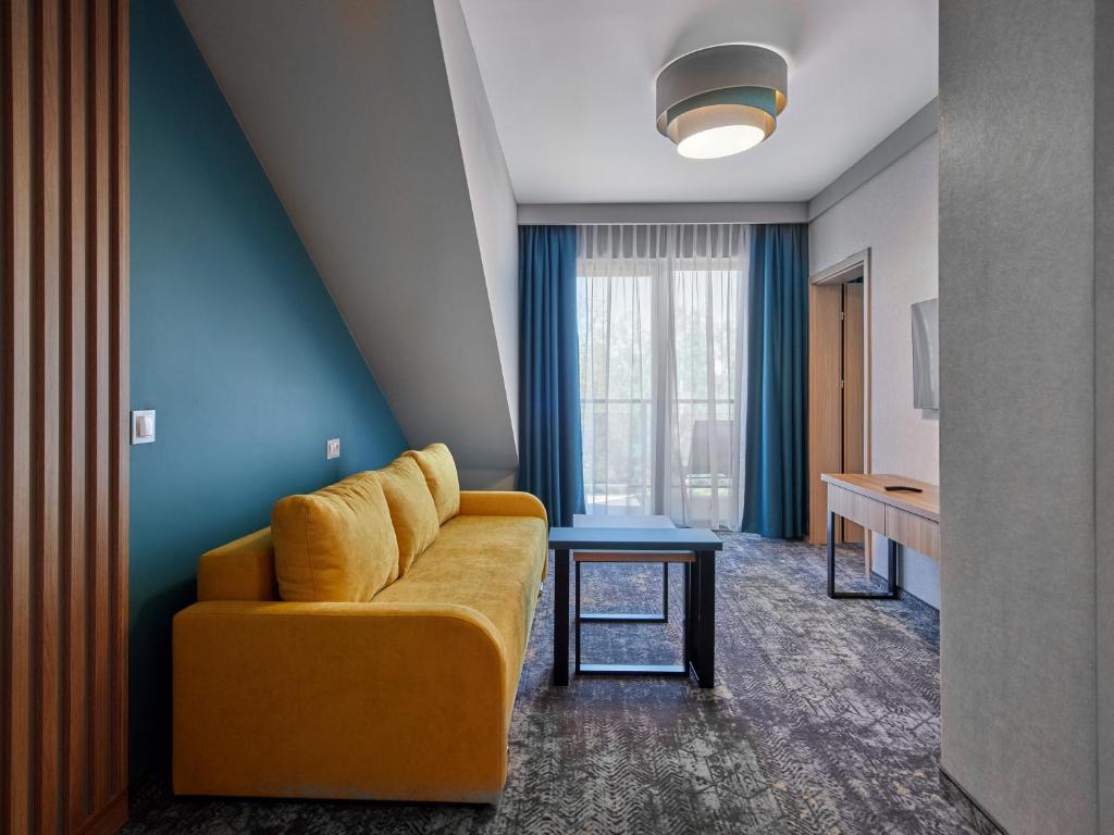 Bright seating area with mustard yellow sofa, teal accent wall, coffee tables, balcony doors.