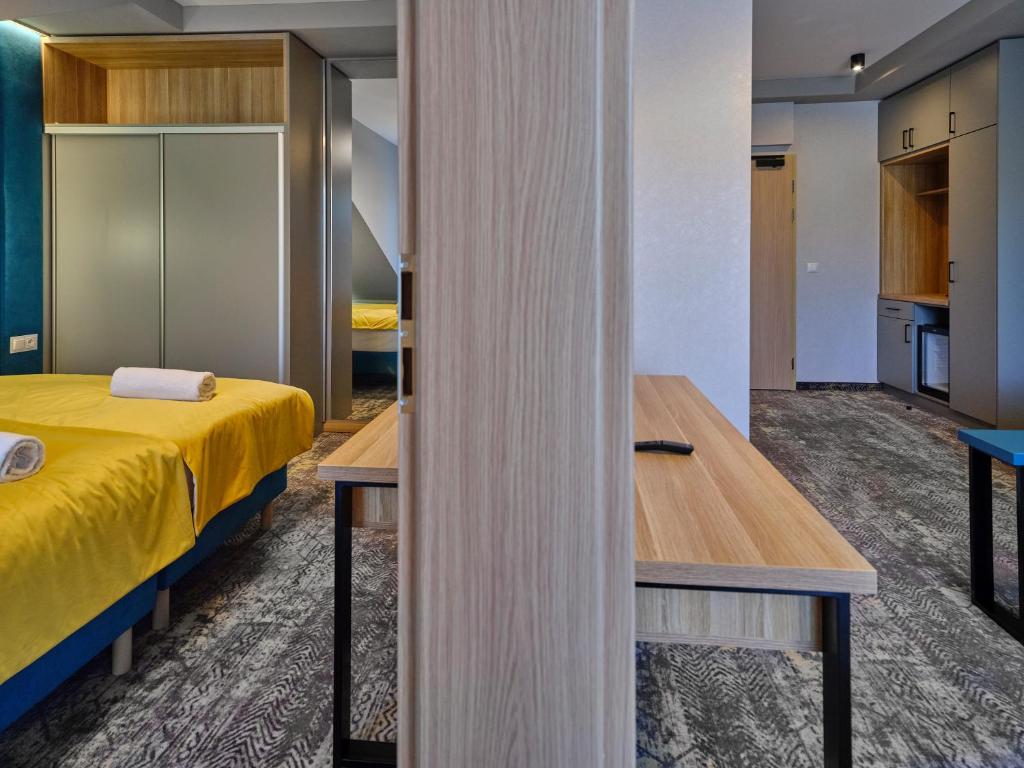 Split view showing bedroom with yellow bedding left and kitchenette entrance right, wooden divider.