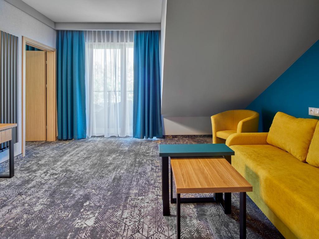 Spacious suite living area with yellow sofa, matching armchair, blue curtains, wooden nesting tables.