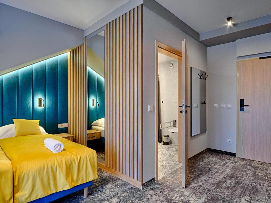 Compact room with bright yellow bedding, teal upholstered headboard, mirrored divider and open bathroom door.