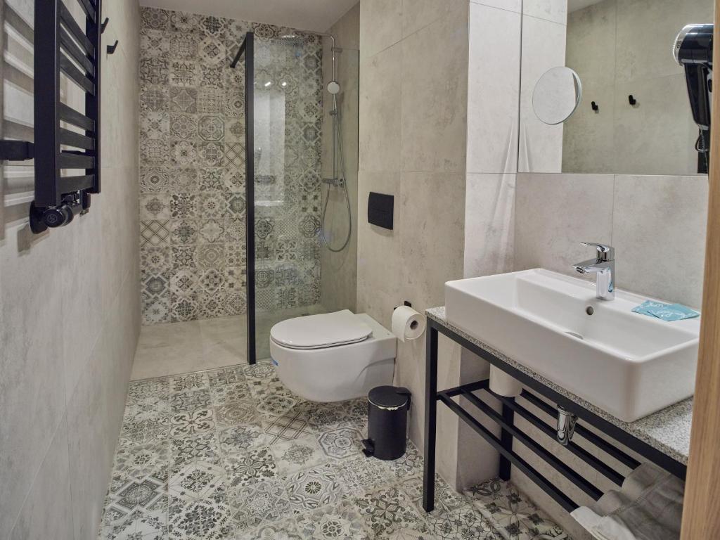 Modern bathroom with patterned tile floor and shower, wall-mounted toilet and sink on metal frame.
