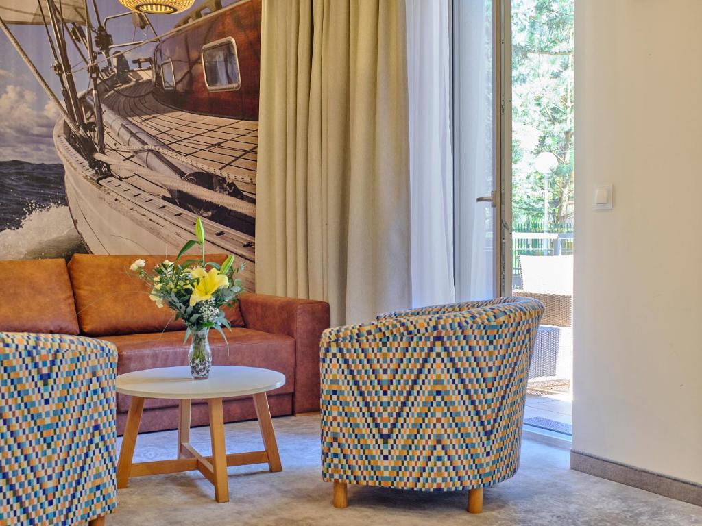 Sunlit lounge corner with patterned armchairs, round table holding fresh flowers, brown sofa and nautical mural.