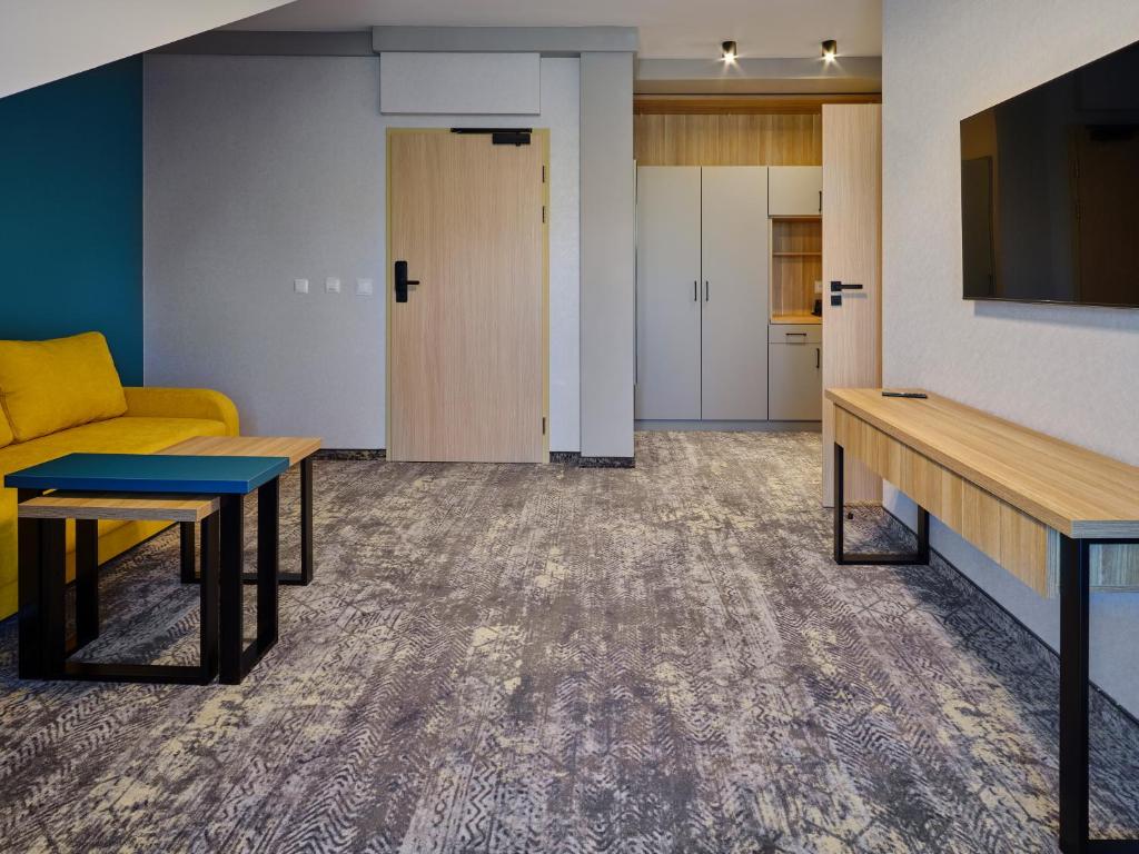 Suite entrance view showing yellow sofa left, nested tables, wall TV, wardrobe by door.