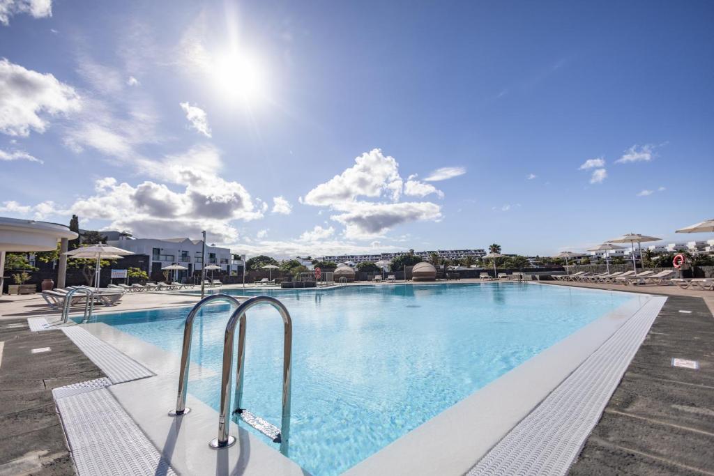 a large swimming pool with blue water and chairs at Caybeach Papagayos in Playa Blanca