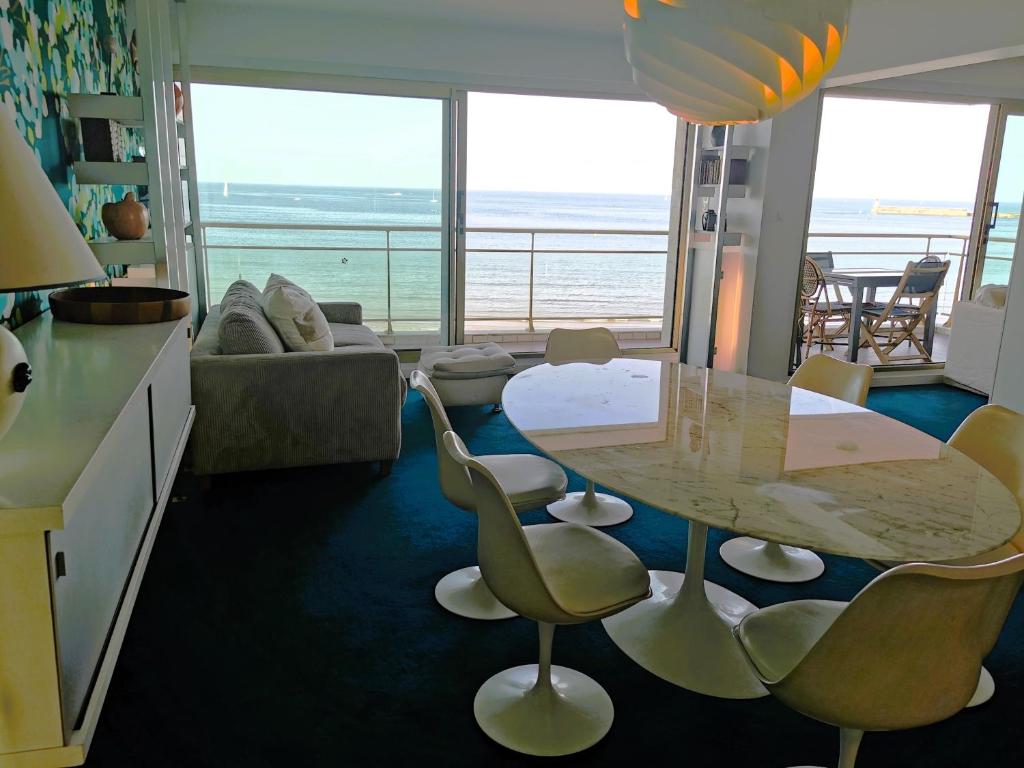 - un salon avec une table et des chaises offrant une vue sur l'océan dans l'établissement Les Soleils, à Les Sables-dʼOlonne