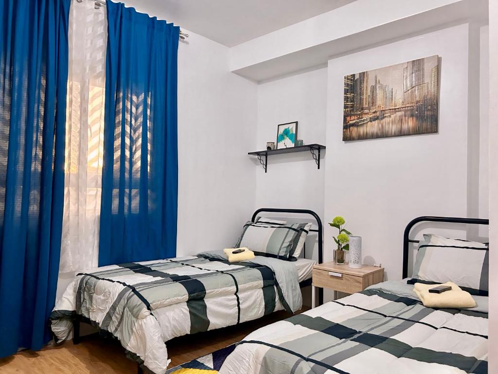 two beds in a room with blue curtains at Mesaverte Residences Cozy Studio Unit in Cagayan de Oro