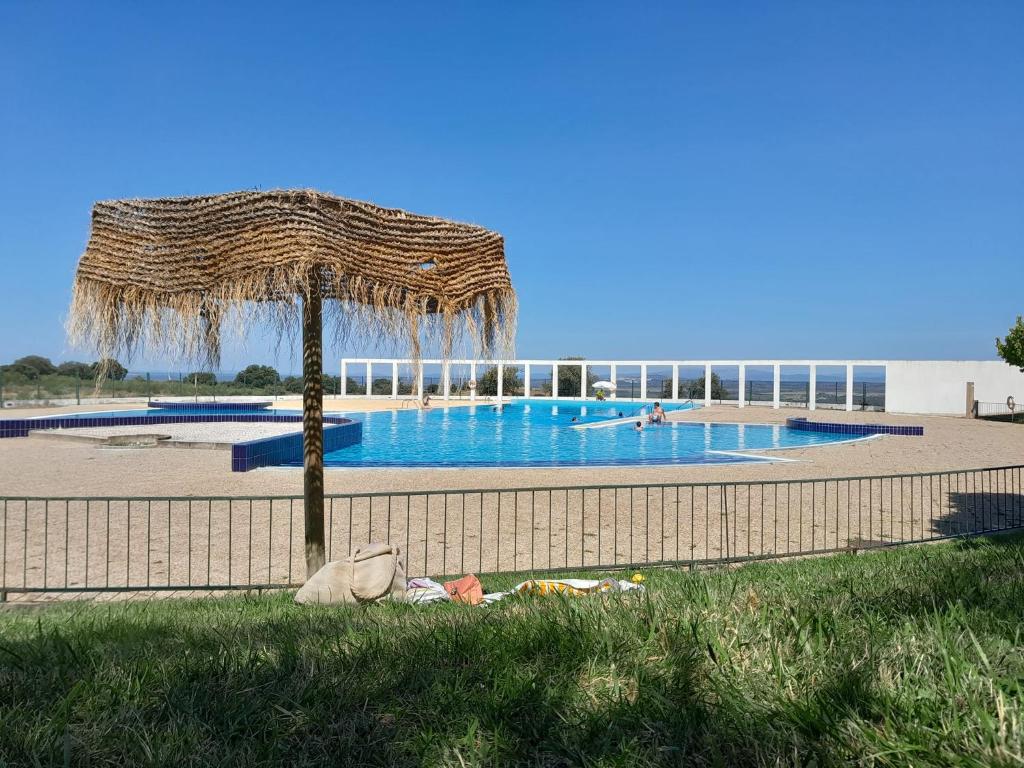 uma piscina com um guarda-sol de palha ao lado de uma cerca em Cantinho D'Avó Maria em Zebreira
