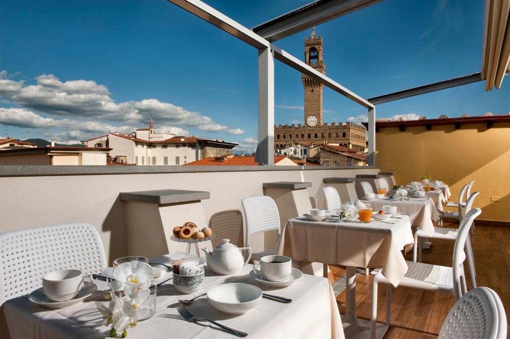 un restaurante con mesas y sillas blancas y una torre del reloj en Hotel della Signoria, en Florencia