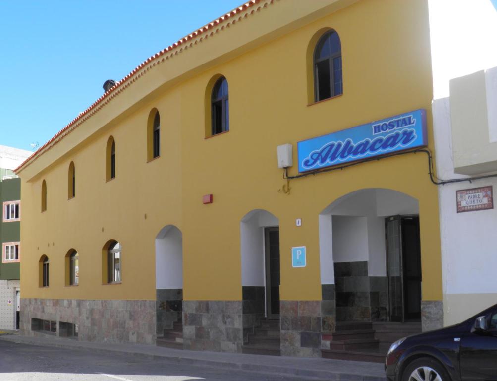 a yellow building with a blue sign on it at Hostal Albacar in Melenara