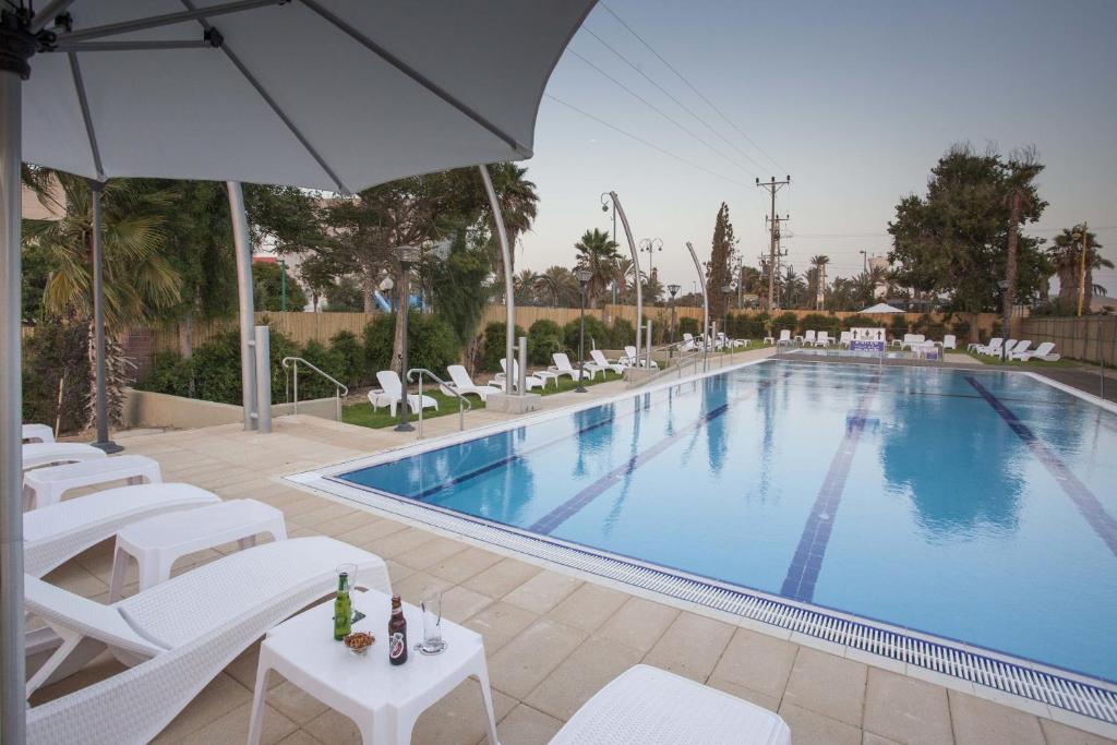 a swimming pool with white chairs and an umbrella at Desert Iris Hotel in Yeroẖam
