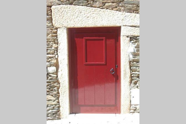 een rode deur in een gebouw met een stenen muur bij Casa da Caroline in Freixo de Espada à Cinta