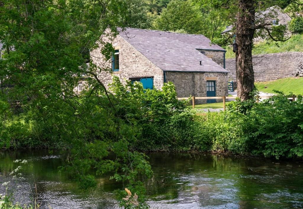 une maison en pierre avec une porte bleue à côté d'une rivière dans l'établissement Kingfisher Cottage Upperdale Peak District, à Buxton