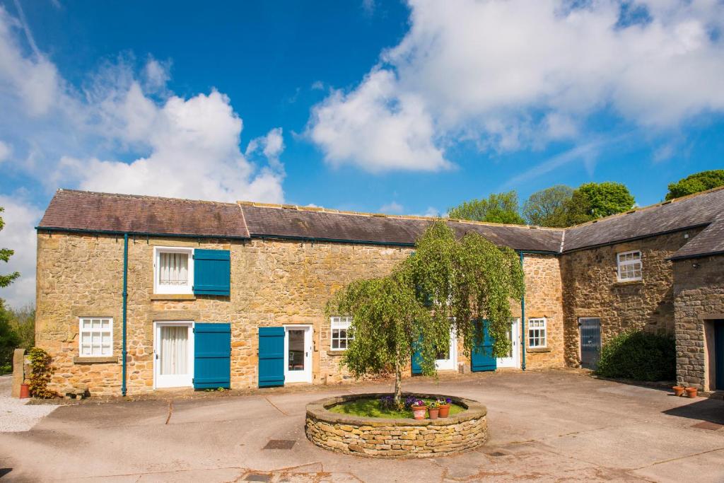 a large brick building with blue doors and a tree in a courtyard at Edensor Cottage Bakewell Peak District in Bakewell