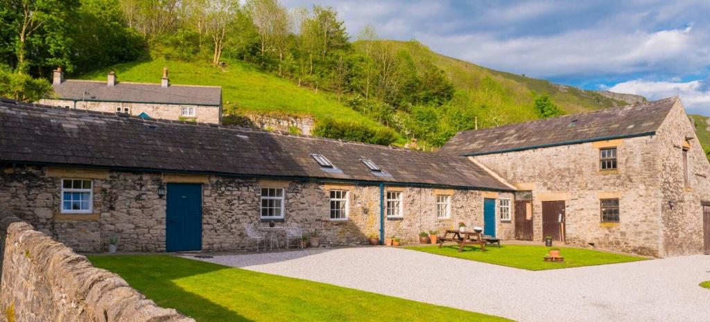 une vieille maison en pierre avec une colline verdoyante en arrière-plan dans l'établissement Heron Cottage Upperdale Peak District, à Buxton