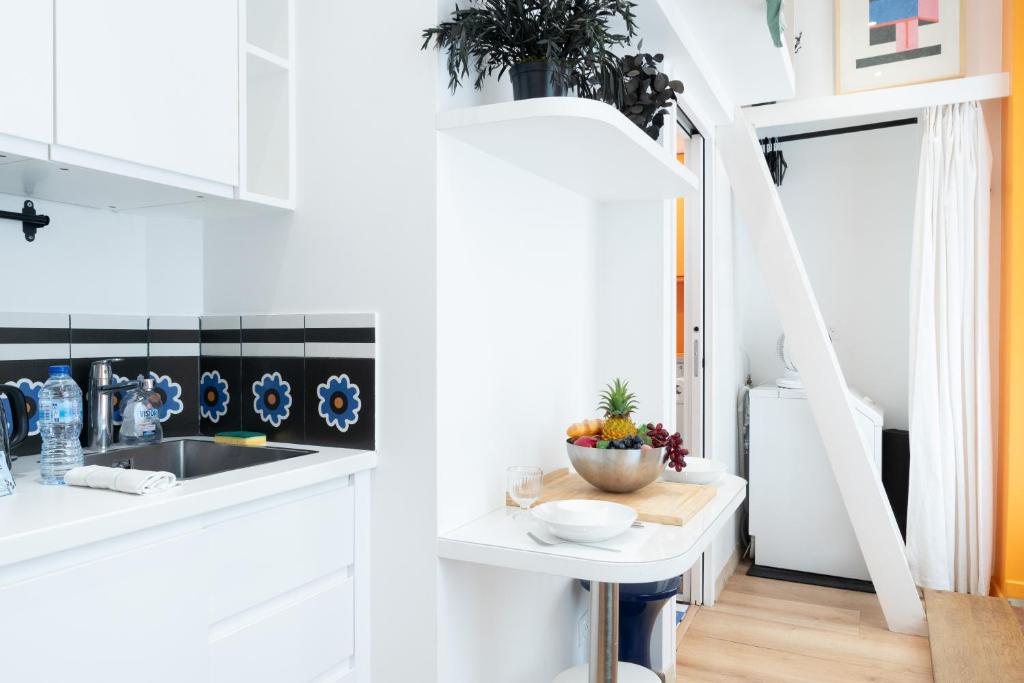- une cuisine avec des placards blancs et une table avec un bol de fruits dans l'établissement Lavie Maison Petite Studio, à Paris