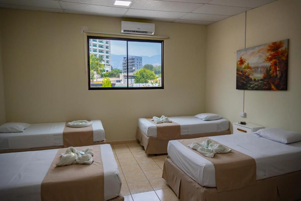 a room with four beds and a window at Hotel La Capilla - Suites & Apartments San Benito in San Salvador