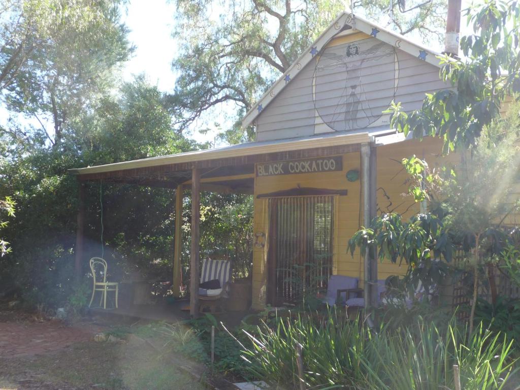 uma pequena casa amarela com um alpendre e uma cadeira em Black Cockatoo Lodge em Nannup